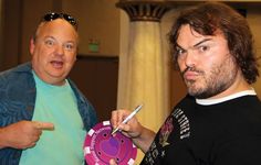 two men standing next to each other pointing at a paper plate with a pig on it