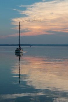 a sailboat floating on top of a lake under a colorful sky with clouds in the background