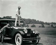 an old black and white photo of two men cleaning the hood of a vintage car