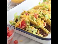 two tacos with shredded cheese and lettuce are on a plate next to a bowl of tomatoes