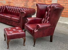 a red leather couch and chair sitting next to each other in front of a brick wall