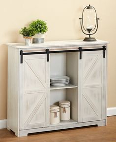 a white cabinet with two doors and plates on it next to a potted plant