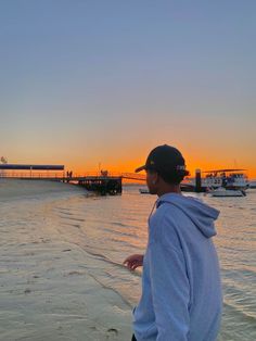 a man standing on top of a sandy beach next to the ocean at sun set