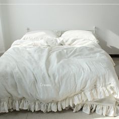 an unmade bed with white linens and ruffled bedspread on the floor