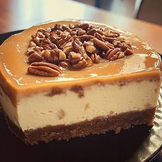 a piece of cheesecake with pecans on top is sitting on a black plate