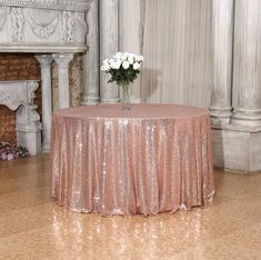 a table with a pink sequined cloth on it and white flowers in a vase