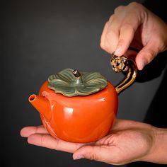 a person holding an orange teapot with a gold decoration on it's handle