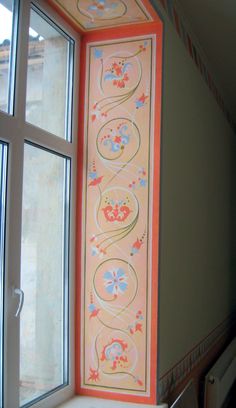 an open window in a room with flowers painted on the wall and below it is a decorative panel