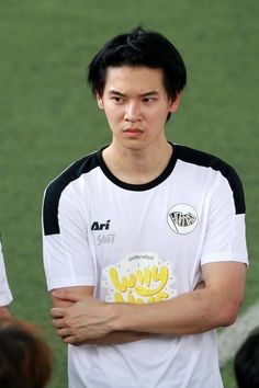 a young man standing on top of a soccer field wearing a white shirt and holding his arms crossed