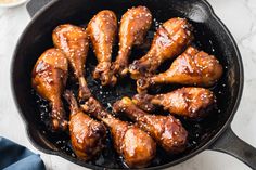 chicken wings are cooking in a skillet with sesame seeds and seasoning on the side