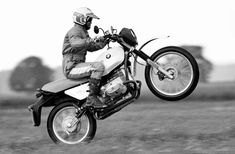 a man riding on the back of a motorcycle in mid air over a grass covered field