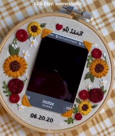 an embroidered photo frame with sunflowers and roses in the center on a checkered tablecloth