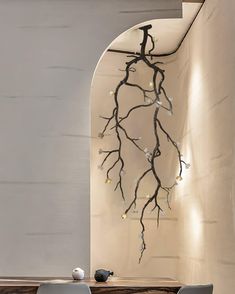 a dining room table with two chairs and a wall decoration behind it that has branches hanging from the ceiling