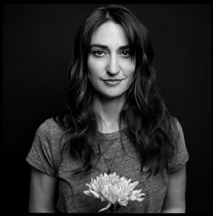 a black and white photo of a woman with long hair holding a flower in her hands