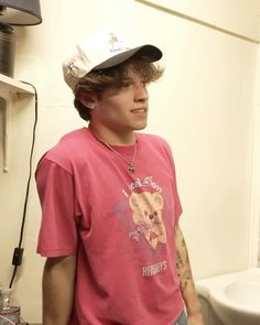 a young man wearing a pink shirt and hat standing in front of a white toilet