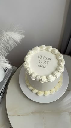 a white cake sitting on top of a table next to a vase with flowers and feathers