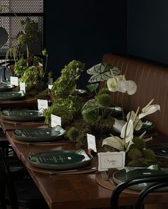 a long table with place cards and plates on it, along with plants in the center