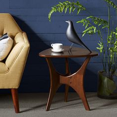 two chairs and a table with a coffee cup on it in front of a blue wall