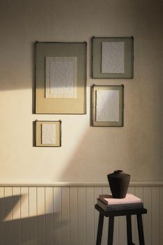 three framed pictures hang on the wall above a stool in a room with white paneling