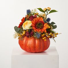 an orange pumpkin filled with flowers and greenery