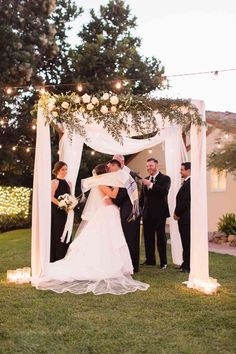 a bride and groom kissing under an outdoor wedding ceremony arch with fairy lights on the side