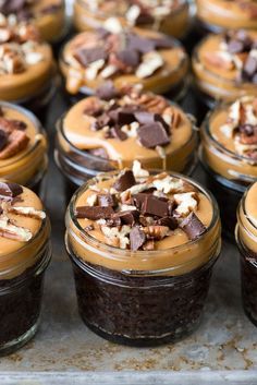 many desserts are in small glass jars on a tray with nuts and chocolate toppings