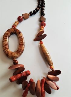 a long necklace with various beads and wood pieces on it's sides, hanging from a white surface