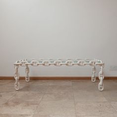 a white bench sitting on top of a tile floor next to a wall with chains hanging from it's sides