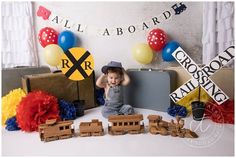 a little boy sitting on top of a table next to train decorations and suitcases