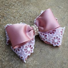 two pink bows with white lace and pearls on the ends are laying on a stone surface