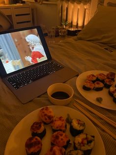 an open laptop computer sitting on top of a bed next to plates of sushi