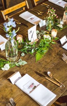 the table is set with place settings and flowers in vases on each side, along with silverware