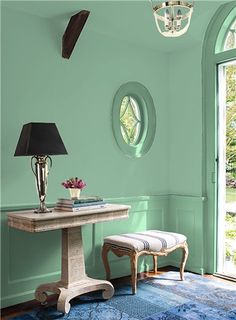 a room painted in green and blue with a table, chair, lamp and rug