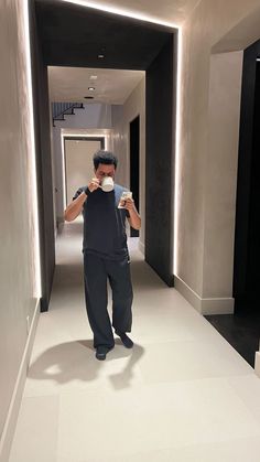 a man standing in a hallway drinking from a cup