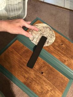 a person is holding a piece of paper on top of a wooden table with a fan