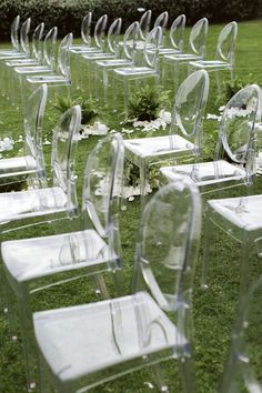 rows of clear chairs sitting on top of a lush green field