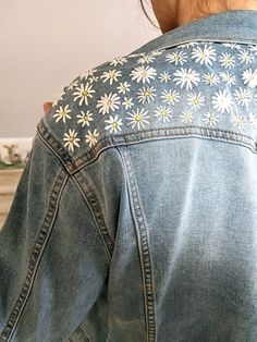 the back of a woman's jean jacket with white daisies on it,