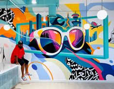 a man sitting in front of a colorful wall with large sunglasses on it's face