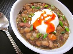 a white bowl filled with beans and sour cream on top of a black table next to a spoon