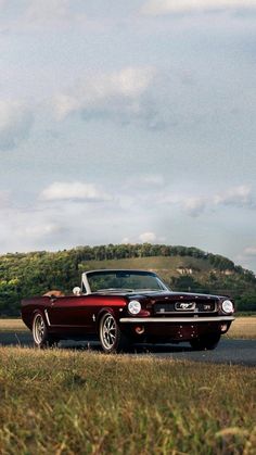 a red convertible car parked on the side of a road in front of a hill