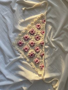 a white shirt with pink flowers is laying on top of the bed and it's crocheted