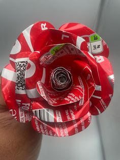 a red flower made out of coca - cola cans is being held by someone's hand