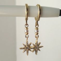 These Dainty North Star Earrings, featuring a starburst design, are perfect for any occasion. Easy to wear and striking in appearance, these earrings are an ideal gift for birthdays, anniversaries, bridesmaids, friends, sisters, and as a Christmas present. The combination of cubic zirconia and Swarovski pearls adds a touch of glamour, making these earrings a delightful addition to any jewelry collection. Details: Earring Hooks: Huggie Hoop. Material: 14k thick gold plated over brass. Stones: Cub Dainty Star Charm Drop Earrings, Gold Drop Earrings With Star Charm, Star-shaped Pearl Drop Earrings As Gift, Celestial Drop Earrings With Star Charm, Earrings Starburst, Sparkling Star-shaped Celestial Earrings, Celestial Star-shaped Sparkling Earrings, Elegant Star-shaped Gold Plated Earrings, Gold Star-shaped Crystal Earrings For Pierced Ears