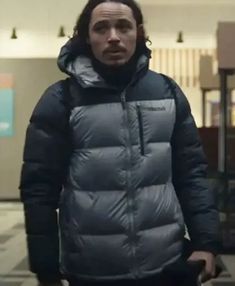 a man with long hair wearing a black and grey puffy jacket in a hallway