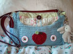 a crocheted purse with buttons and a stuffed animal on the side, sitting on a bed