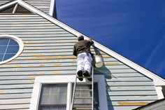 a man on a ladder painting the side of a house with blue skies in the background