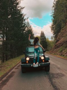 a woman sitting on the hood of a jeep waving to someone in the back seat