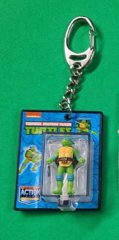 a keychain with a toy figure in it on a green surface next to a pair of scissors