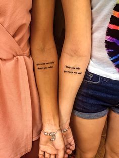 two girls with matching tattoos on their arms, both have words written on the arm