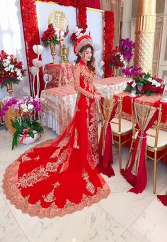 a woman in a red and gold wedding dress standing next to a table with flowers on it